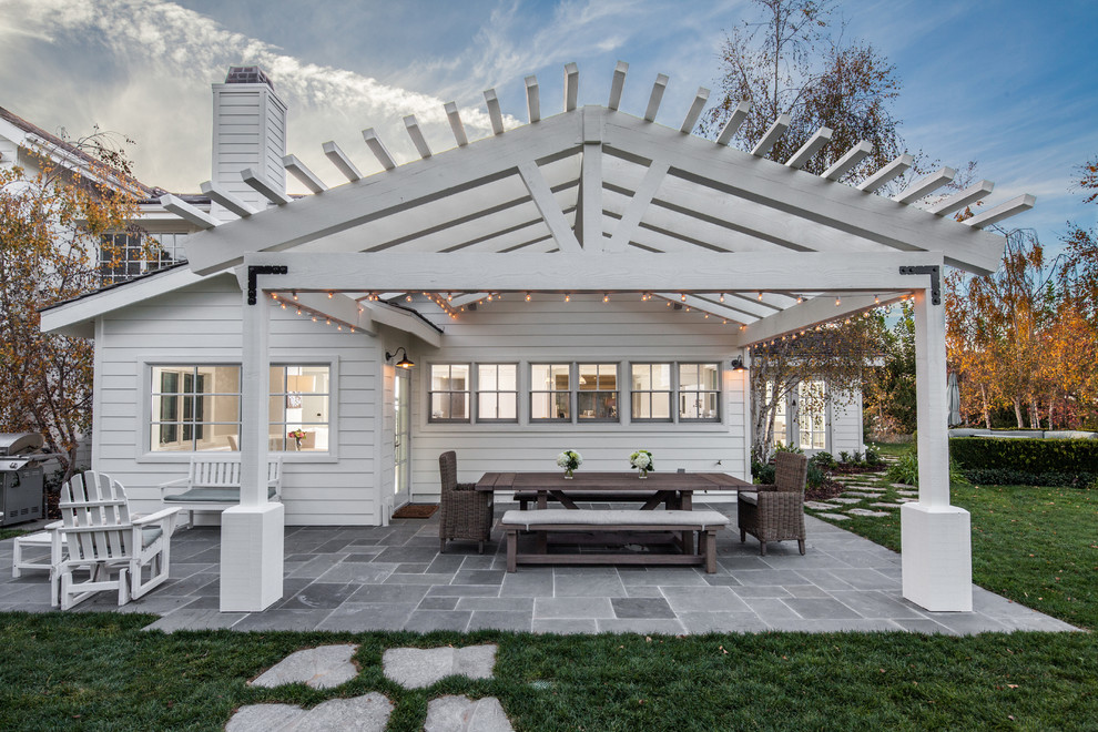 This is an example of a mid-sized country backyard patio in San Diego with natural stone pavers and a pergola.