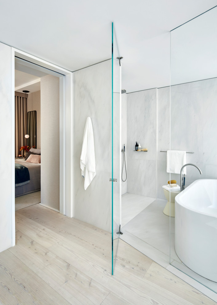 This is an example of a large contemporary master wet room bathroom in New York with a freestanding tub, white tile, marble, white walls, light hardwood floors, beige floor and a hinged shower door.