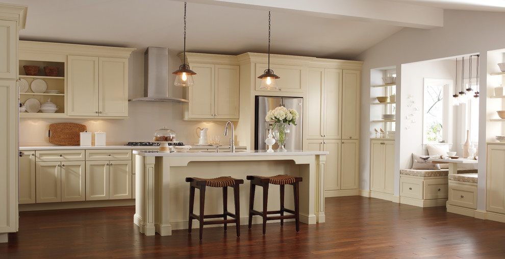 This is an example of a large traditional l-shaped eat-in kitchen in Boston with white splashback, stainless steel appliances, dark hardwood floors, with island, an undermount sink, recessed-panel cabinets, yellow cabinets, solid surface benchtops, brown floor and white benchtop.