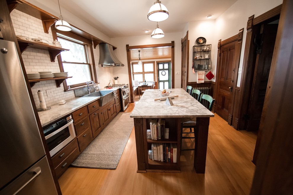 Inspiration for a traditional u-shaped kitchen in Cedar Rapids with a farmhouse sink, beaded inset cabinets, medium wood cabinets, granite benchtops, white splashback, subway tile splashback, stainless steel appliances, medium hardwood floors and with island.