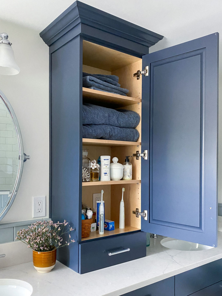 Пример оригинального дизайна: главная ванная комната в стиле кантри с фасадами в стиле шейкер, синими фасадами, отдельно стоящей ванной, угловым душем, раздельным унитазом, белой плиткой, керамической плиткой, белыми стенами, полом из керамогранита, врезной раковиной, столешницей из искусственного кварца, бежевым полом, душем с распашными дверями, бежевой столешницей, сиденьем для душа, тумбой под две раковины и встроенной тумбой