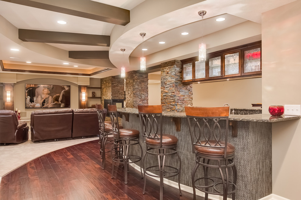 Photo of a mid-sized traditional u-shaped seated home bar in Minneapolis with an undermount sink, glass-front cabinets, dark wood cabinets, limestone benchtops, green splashback, stone tile splashback, dark hardwood floors, brown floor and brown benchtop.