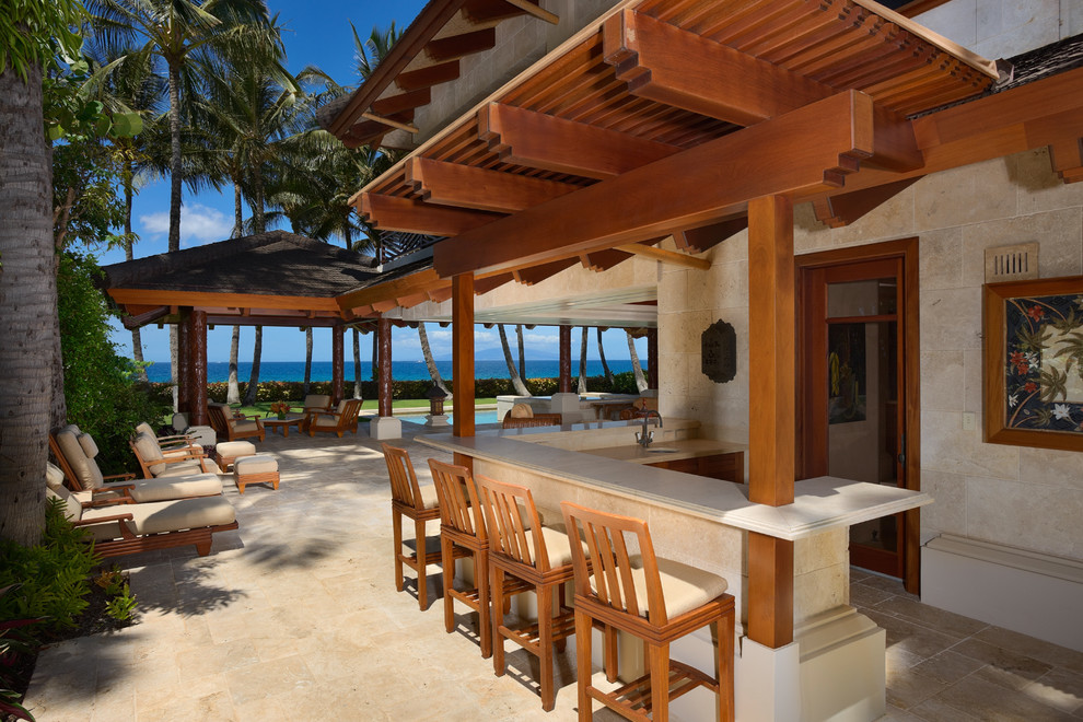 Photo of an expansive tropical backyard patio in Hawaii with a gazebo/cabana and natural stone pavers.