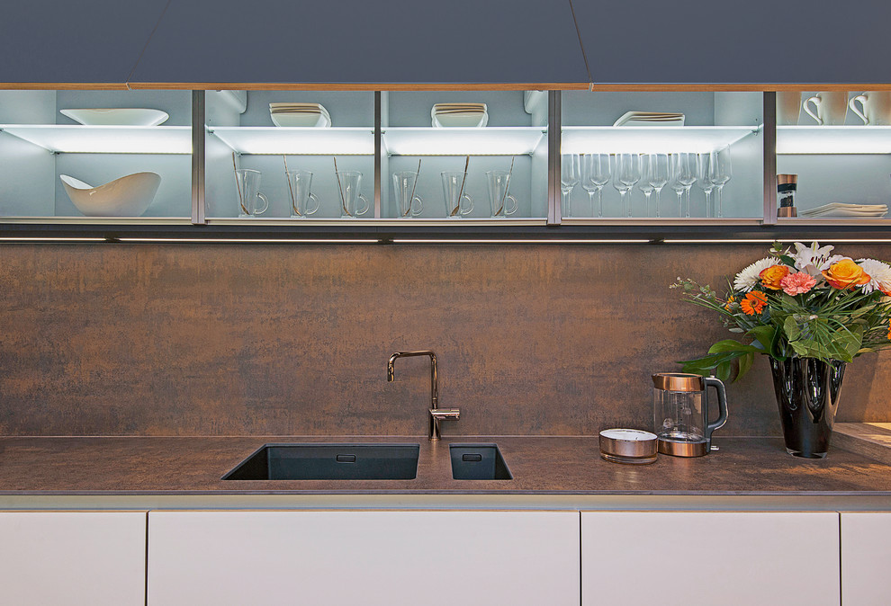 Inspiration for a mid-sized contemporary single-wall eat-in kitchen in London with a drop-in sink, flat-panel cabinets, white cabinets, solid surface benchtops, metallic splashback, panelled appliances, medium hardwood floors and a peninsula.