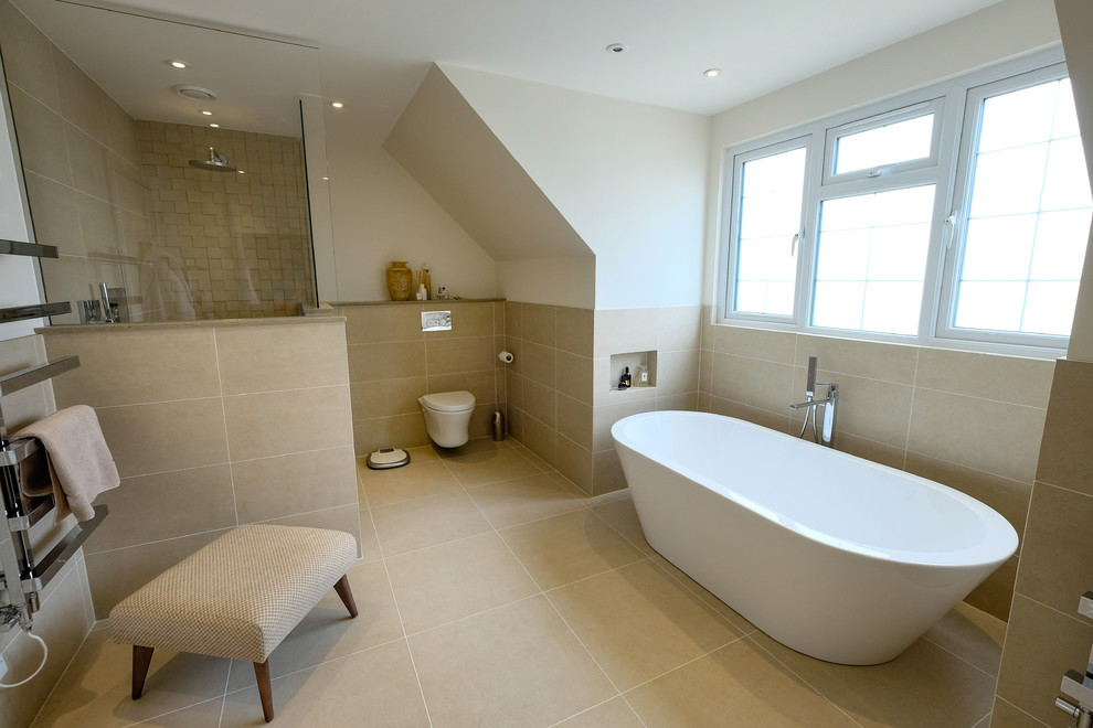 This is an example of a large contemporary master bathroom in Hertfordshire with flat-panel cabinets, medium wood cabinets, a freestanding tub, an open shower, a wall-mount toilet, beige tile, mosaic tile, beige walls, porcelain floors, a console sink, limestone benchtops, beige floor, an open shower and beige benchtops.