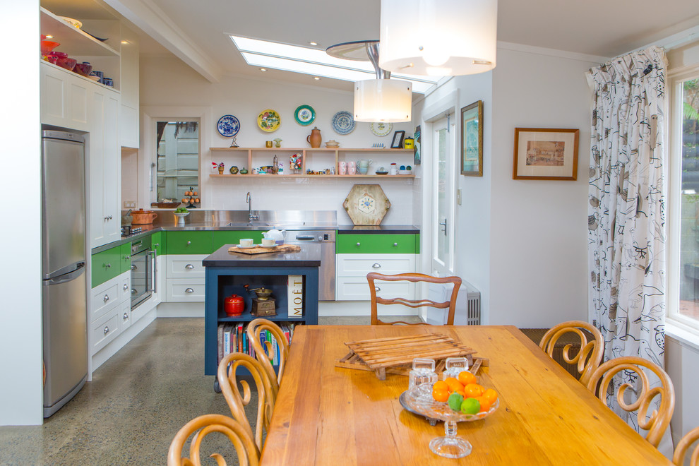 Inspiration for a small eclectic l-shaped eat-in kitchen in Wellington with a double-bowl sink, open cabinets, stainless steel benchtops, white splashback, ceramic splashback, stainless steel appliances and with island.