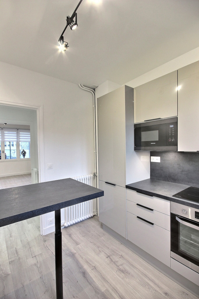 This is an example of a small modern l-shaped kitchen in Paris with a single-bowl sink, beige cabinets, laminate benchtops, black splashback, stainless steel appliances, laminate floors, grey floor and black benchtop.