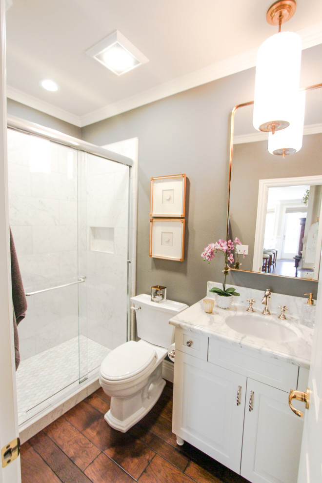 Klassisk inredning av ett litet vit vitt badrum med dusch, med luckor med upphöjd panel, vita skåp, en dusch i en alkov, en toalettstol med separat cisternkåpa, vit kakel, marmorkakel, grå väggar, mörkt trägolv, ett undermonterad handfat, marmorbänkskiva, brunt golv och dusch med skjutdörr