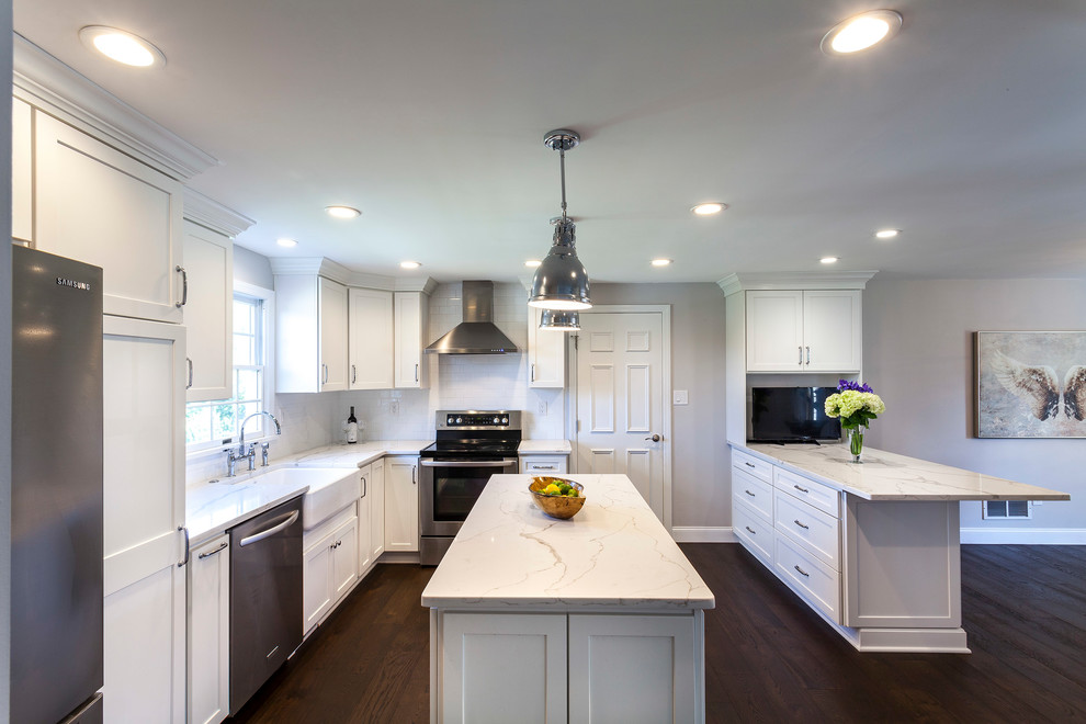 Inspiration for a transitional medium tone wood floor and brown floor kitchen remodel with a farmhouse sink, white cabinets, quartz countertops, white backsplash, ceramic backsplash, stainless steel appliances and an island