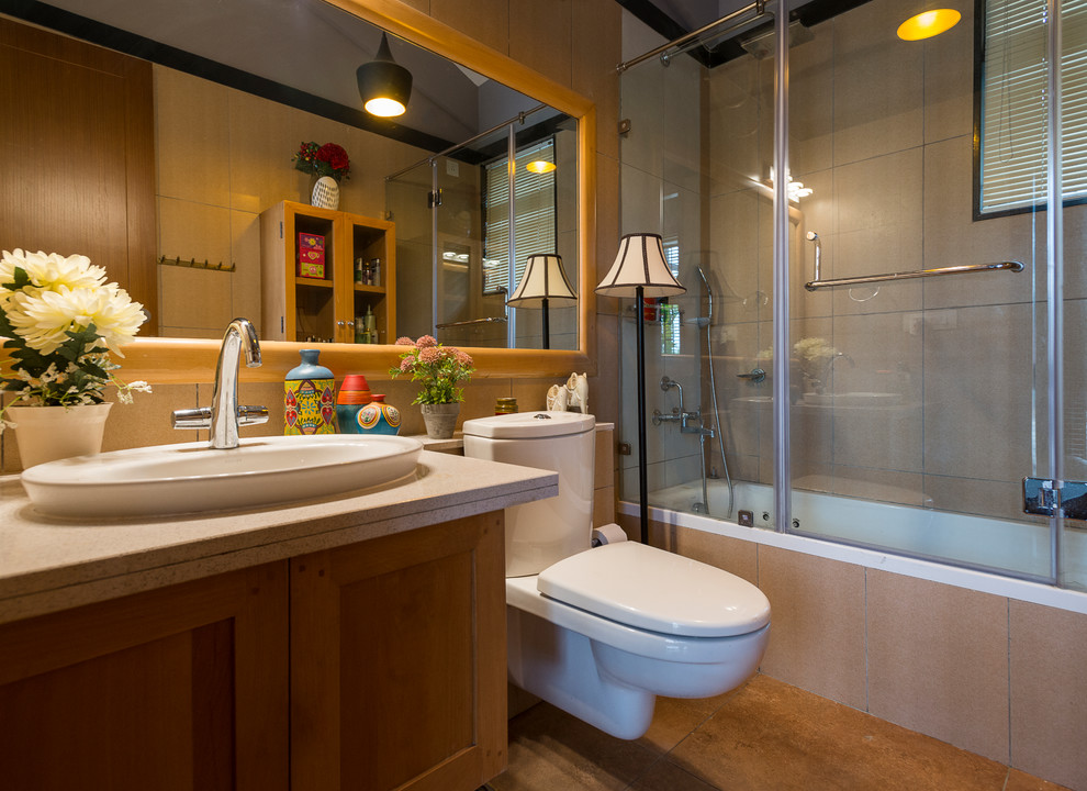 This is an example of a small traditional bathroom in Bengaluru with a two-piece toilet, beige tile, ceramic tile, brown floor, a drop-in sink, shaker cabinets, medium wood cabinets, an alcove tub, a shower/bathtub combo and a hinged shower door.