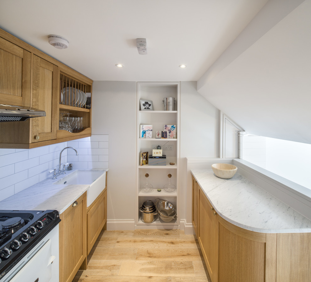 Design ideas for a small contemporary galley kitchen in London with a farmhouse sink, shaker cabinets, light wood cabinets, marble benchtops, white splashback, subway tile splashback, panelled appliances, light hardwood floors and no island.