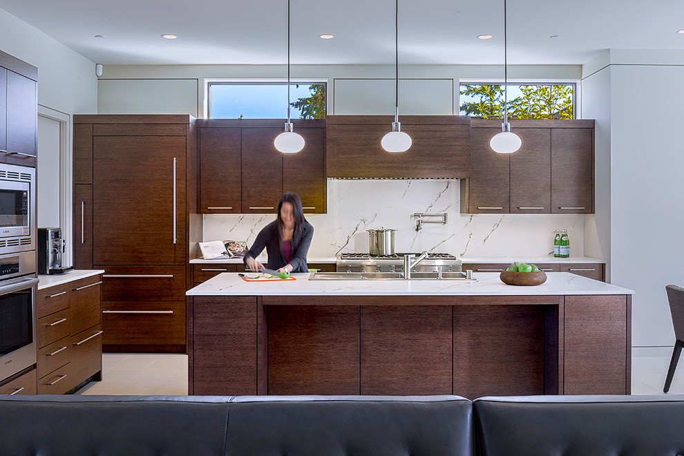 This is an example of a large modern l-shaped kitchen in Seattle with flat-panel cabinets, dark wood cabinets, quartzite benchtops, white splashback, stone slab splashback, with island, white benchtop, porcelain floors, beige floor, a drop-in sink and panelled appliances.