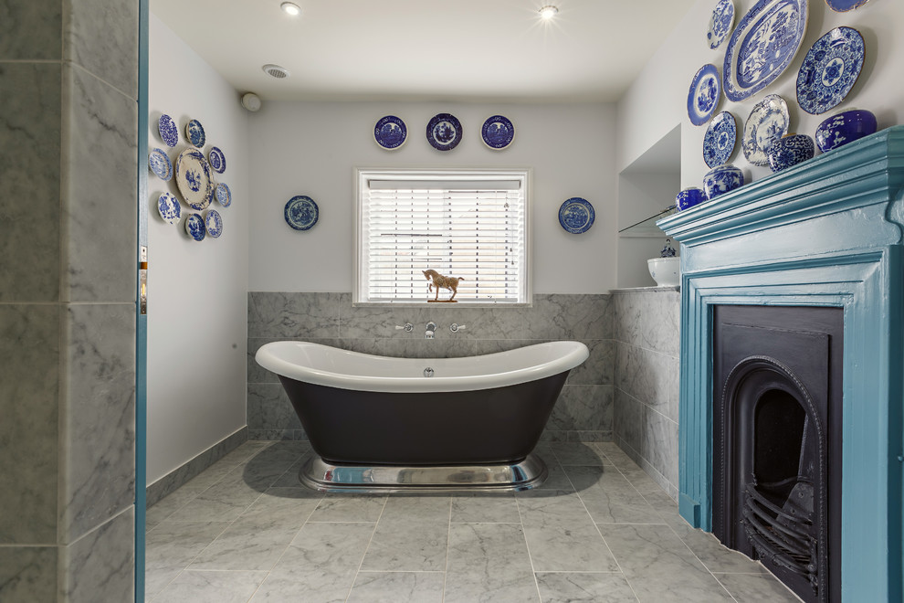 This is an example of a mid-sized eclectic master bathroom in Essex with blue cabinets, a freestanding tub, gray tile, marble, white walls, marble floors and grey floor.