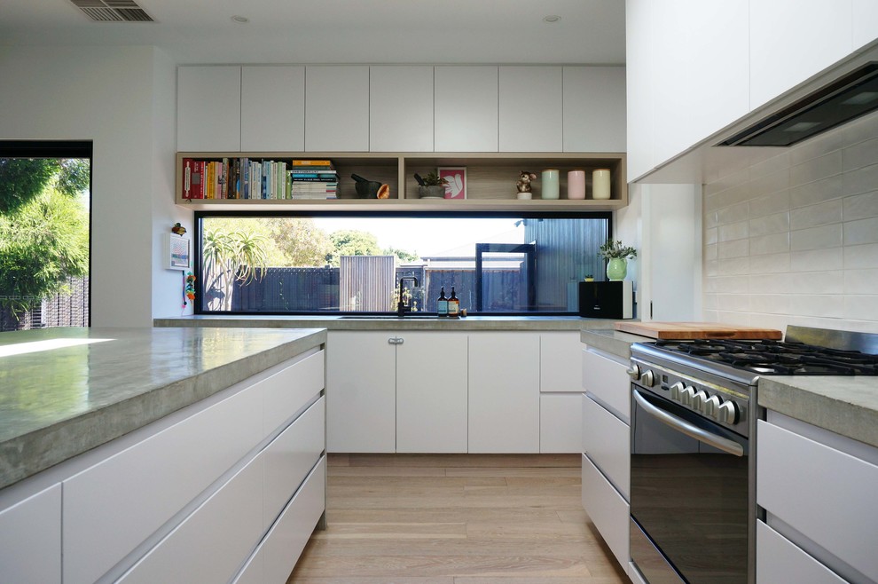 Photo of a modern open plan kitchen in Melbourne with flat-panel cabinets, white cabinets, concrete benchtops, white splashback, with island, an undermount sink, stainless steel appliances and light hardwood floors.