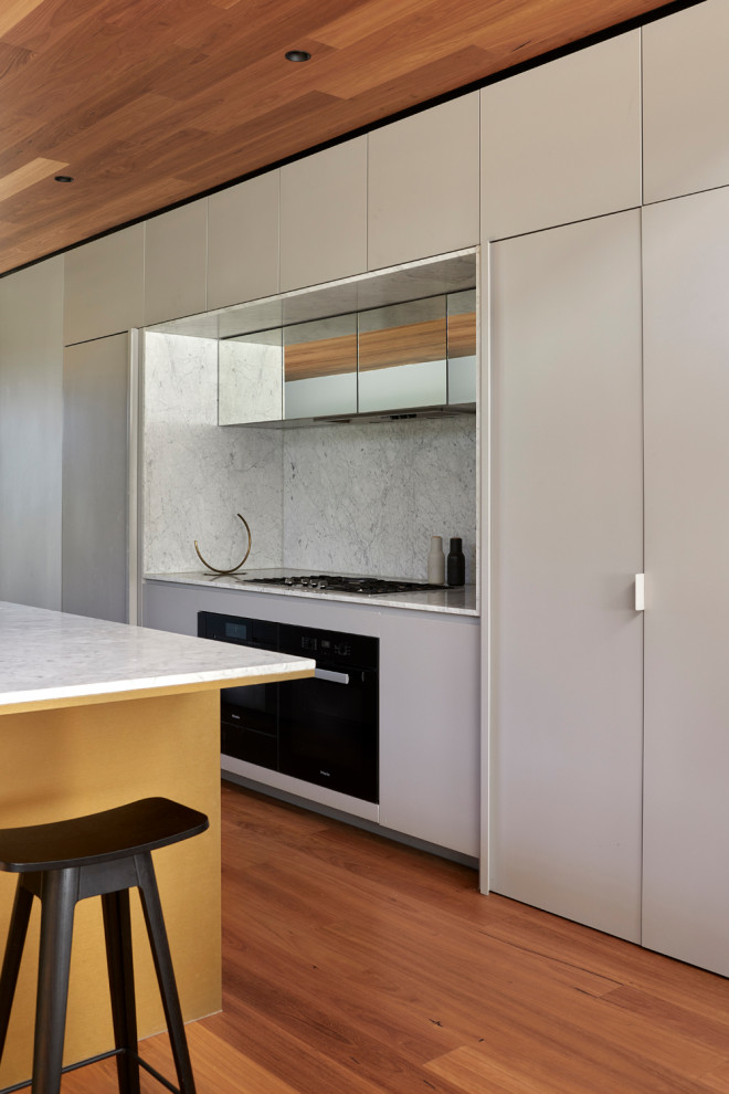 Inspiration for a medium sized contemporary galley open plan kitchen in Melbourne with medium hardwood flooring, a timber clad ceiling, a submerged sink, grey cabinets, marble worktops, marble splashback, black appliances, an island and white worktops.