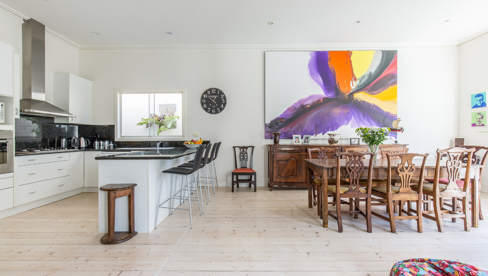 Eclectic u-shaped open plan kitchen in Melbourne with flat-panel cabinets, white cabinets, black splashback, stone slab splashback, stainless steel appliances, light hardwood floors, a peninsula and beige floor.