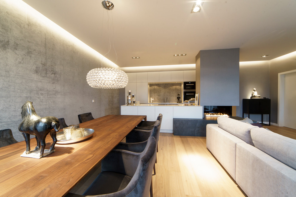 This is an example of a large contemporary open plan dining in Leipzig with grey walls, medium hardwood floors, a plaster fireplace surround, brown floor and a wood stove.