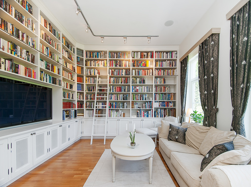 Photo of a traditional enclosed family room in Stockholm with a library, white walls, medium hardwood floors, a wall-mounted tv and brown floor.
