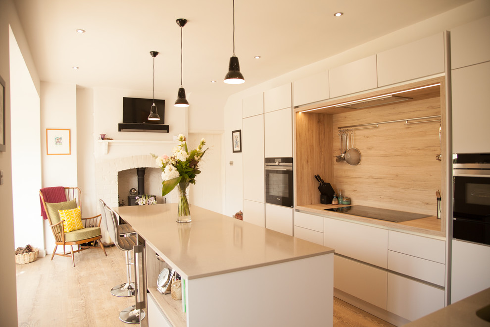 This is an example of a mid-sized scandinavian kitchen in Gloucestershire with flat-panel cabinets, white cabinets, timber splashback, with island, beige floor, beige benchtop and black appliances.
