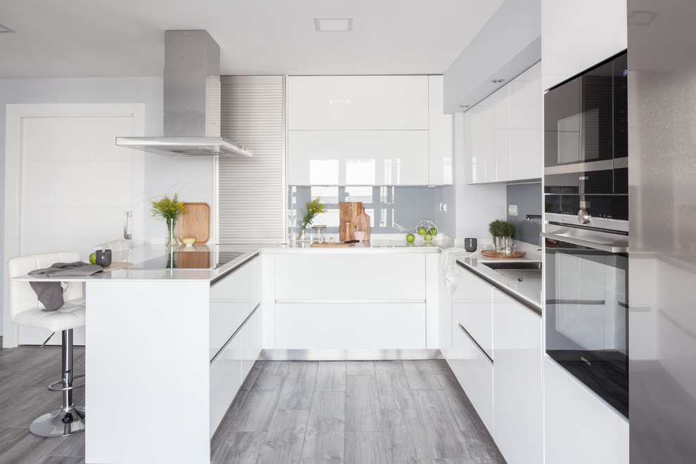 Contemporary u-shaped kitchen in Madrid with an undermount sink, flat-panel cabinets, white cabinets, grey splashback, glass sheet splashback, black appliances, a peninsula, grey floor and white benchtop.