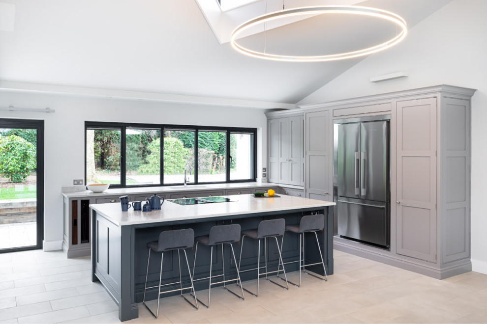Expansive contemporary l-shaped open plan kitchen in Kent with shaker cabinets, quartzite benchtops, porcelain floors, with island, grey floor, a farmhouse sink, grey cabinets, grey splashback, granite splashback, stainless steel appliances, white benchtop and vaulted.