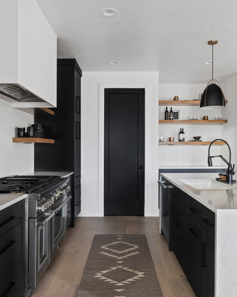 This is an example of a mid-sized scandinavian l-shaped open plan kitchen in Boise with an undermount sink, flat-panel cabinets, black cabinets, quartzite benchtops, white splashback, subway tile splashback, stainless steel appliances, light hardwood floors, with island, beige floor, white benchtop and exposed beam.