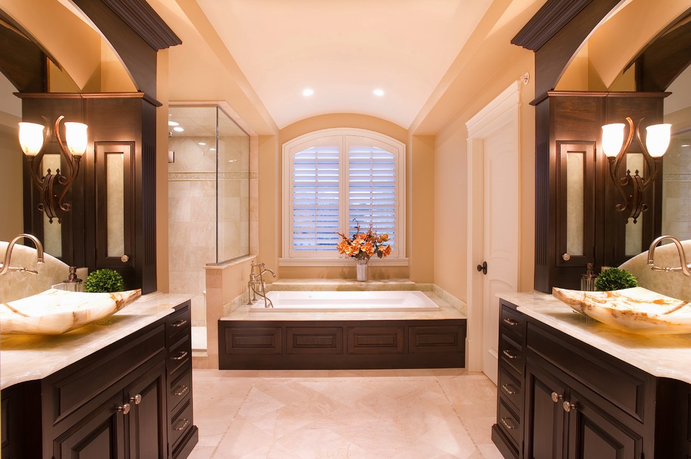 Inspiration for a large traditional master bathroom in Chicago with a vessel sink, dark wood cabinets, marble benchtops, a corner shower, beige walls, a drop-in tub, travertine, porcelain floors, beige floor and a hinged shower door.