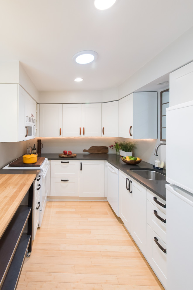 Mid-sized contemporary galley open plan kitchen in Portland with an undermount sink, shaker cabinets, white cabinets, granite benchtops, white splashback, white appliances, bamboo floors, with island, beige floor and grey benchtop.