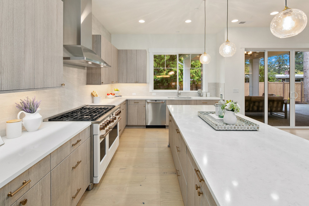 Photo of a large rural l-shaped kitchen/diner in Seattle with a built-in sink, flat-panel cabinets, grey cabinets, engineered stone countertops, grey splashback, stone tiled splashback, stainless steel appliances, light hardwood flooring, an island, brown floors and white worktops.