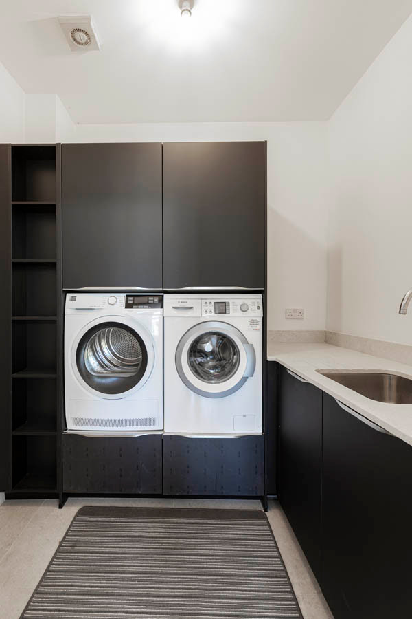 Large modern galley laundry room in Hertfordshire with a single-bowl sink, flat-panel cabinets, black cabinets, concrete benchtops, white splashback, ceramic floors, grey floor and white benchtop.