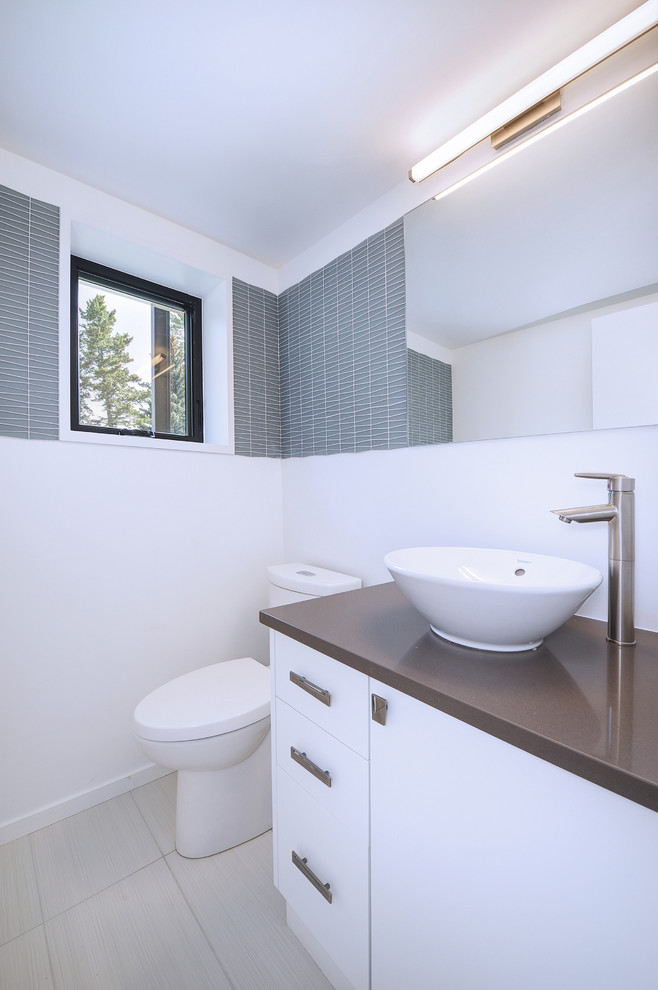 Photo of a small modern powder room in Denver with a one-piece toilet, white walls, ceramic floors, gray tile, glass tile, a vessel sink, beige floor and brown benchtops.