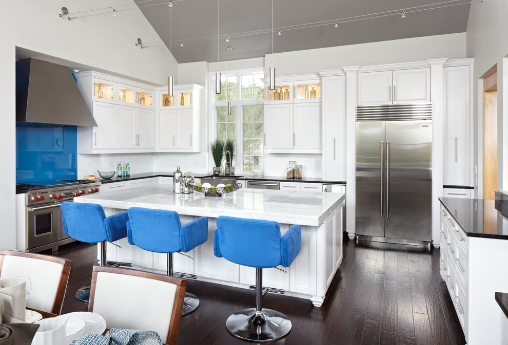 Mid-sized transitional u-shaped eat-in kitchen in Austin with a farmhouse sink, white cabinets, blue splashback, glass sheet splashback, stainless steel appliances, dark hardwood floors, with island, shaker cabinets and solid surface benchtops.