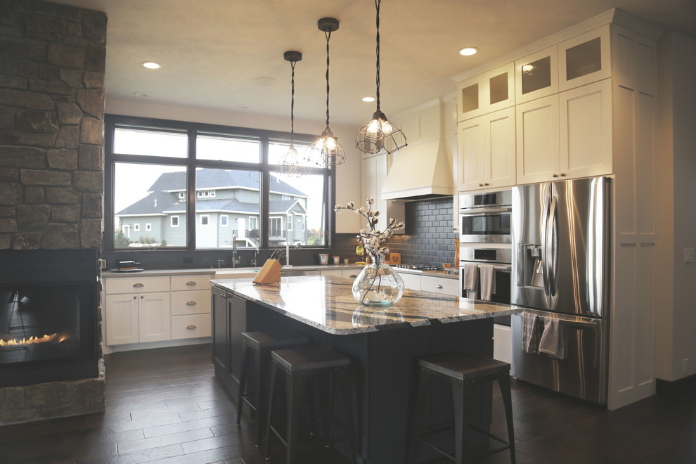 Example of a mid-sized transitional l-shaped dark wood floor eat-in kitchen design with a farmhouse sink, recessed-panel cabinets, white cabinets, granite countertops, black backsplash, porcelain backsplash, stainless steel appliances and an island