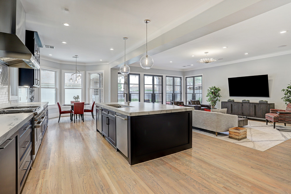 This is an example of a large transitional l-shaped open plan kitchen in Houston with a drop-in sink, recessed-panel cabinets, blue cabinets, quartzite benchtops, white splashback, subway tile splashback, stainless steel appliances, light hardwood floors, with island, brown floor and white benchtop.