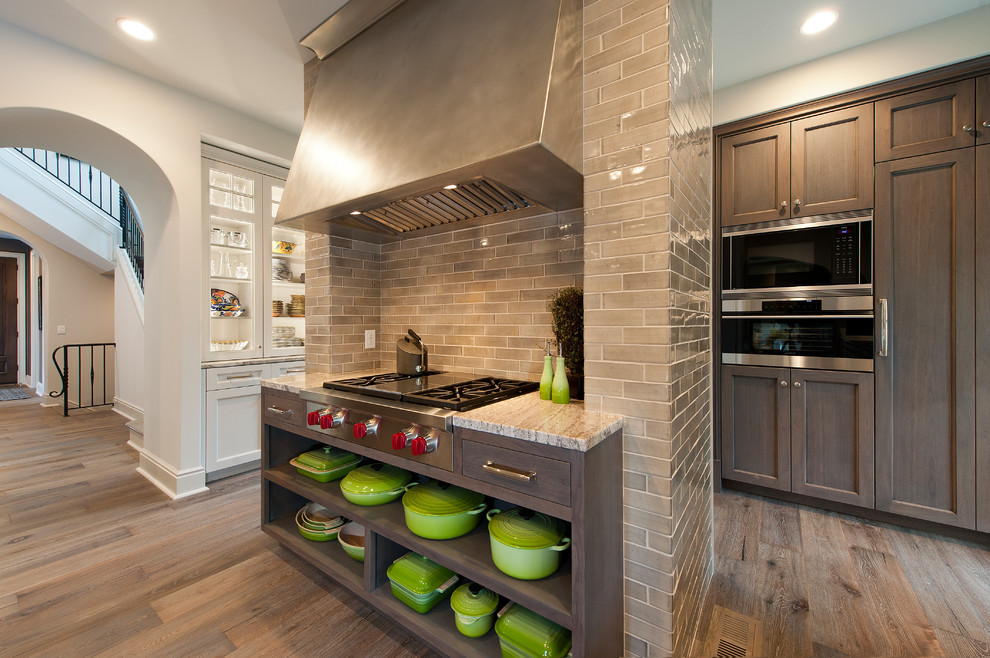 Large transitional medium tone wood floor kitchen pantry photo in Minneapolis with flat-panel cabinets, dark wood cabinets, granite countertops, beige backsplash, subway tile backsplash, paneled appliances and an island