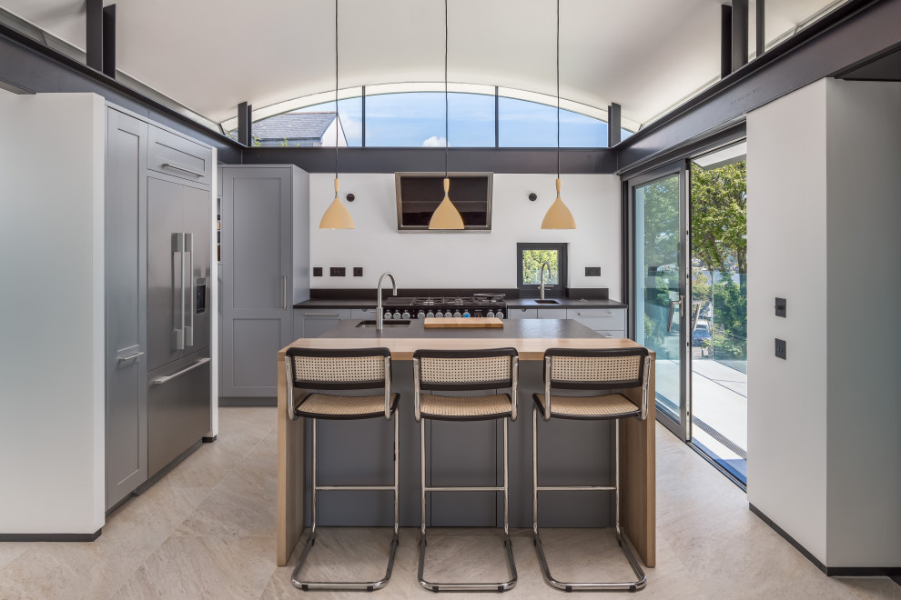 Photo of a mid-sized contemporary kitchen in Cornwall with a drop-in sink, recessed-panel cabinets, grey cabinets, stainless steel appliances, limestone floors, with island and beige floor.