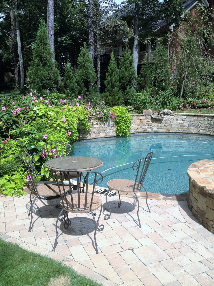 This is an example of a large traditional backyard custom-shaped natural pool in Atlanta with a water feature and natural stone pavers.