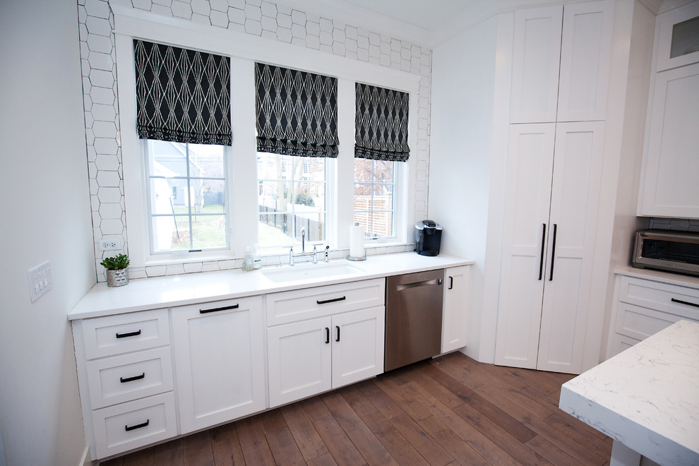 This is an example of a mid-sized transitional u-shaped eat-in kitchen in Chicago with an undermount sink, shaker cabinets, white cabinets, quartz benchtops, white splashback, subway tile splashback, panelled appliances, medium hardwood floors, with island and brown floor.