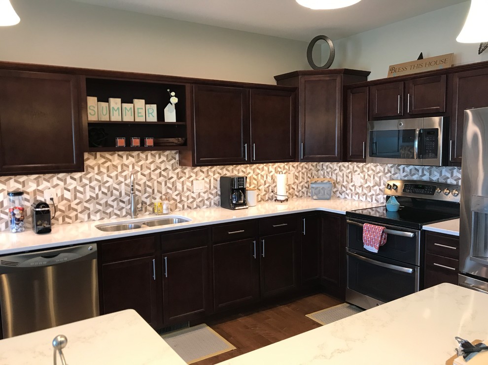 This is an example of a mid-sized contemporary l-shaped open plan kitchen in Cedar Rapids with an undermount sink, flat-panel cabinets, dark wood cabinets, quartz benchtops, multi-coloured splashback, mosaic tile splashback, stainless steel appliances, medium hardwood floors, with island, brown floor and white benchtop.