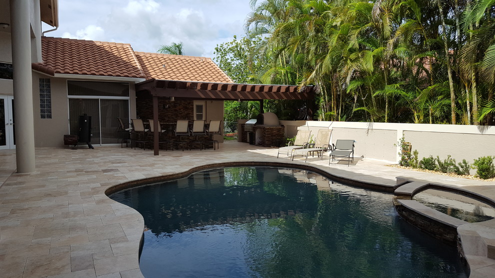 This is an example of a large tropical backyard rectangular natural pool in Miami with a hot tub and natural stone pavers.