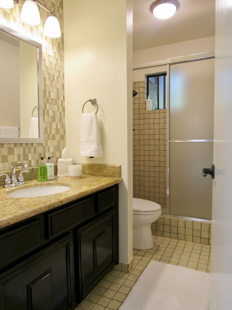 This is an example of a mid-sized country bathroom in San Francisco with dark wood cabinets, a corner shower, a one-piece toilet, green tile, mosaic tile, yellow walls, ceramic floors, a drop-in sink, granite benchtops, yellow floor, a sliding shower screen and brown benchtops.