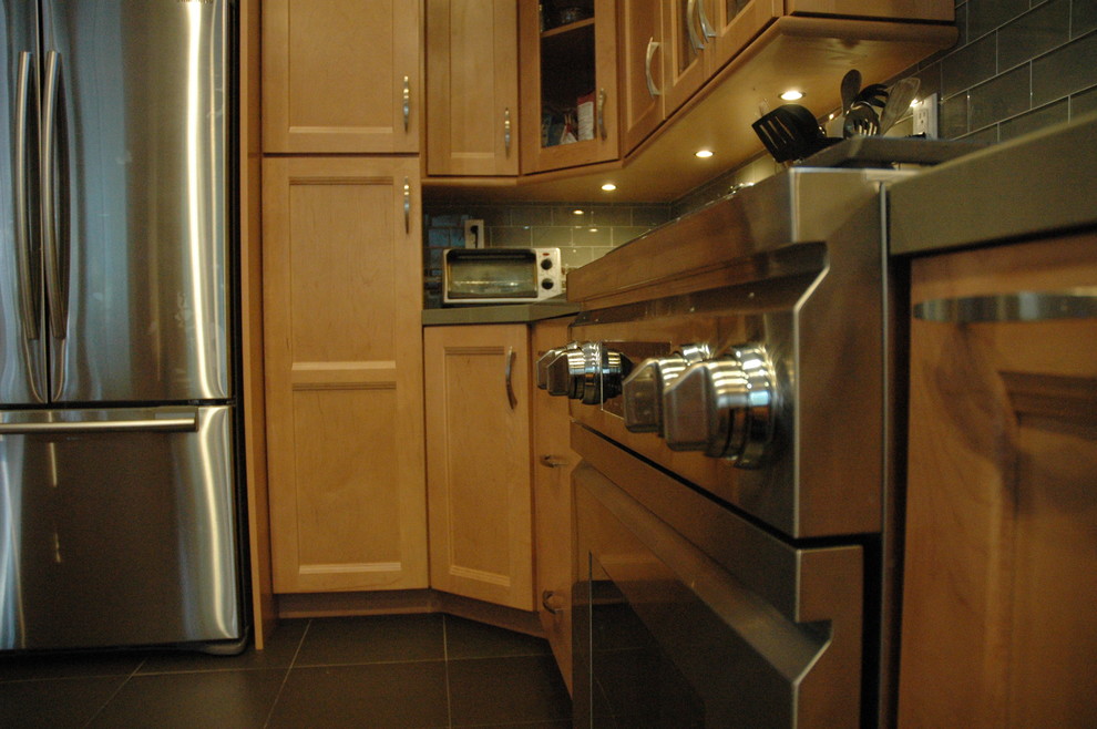 Example of a mid-sized transitional u-shaped slate floor eat-in kitchen design in Orange County with glass-front cabinets, light wood cabinets, quartz countertops, green backsplash, glass tile backsplash, stainless steel appliances and an island