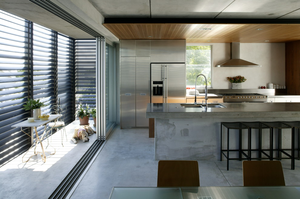 Inspiration for a contemporary galley kitchen in Auckland with a double-bowl sink, flat-panel cabinets, stainless steel cabinets, concrete benchtops, stainless steel appliances, concrete floors and with island.