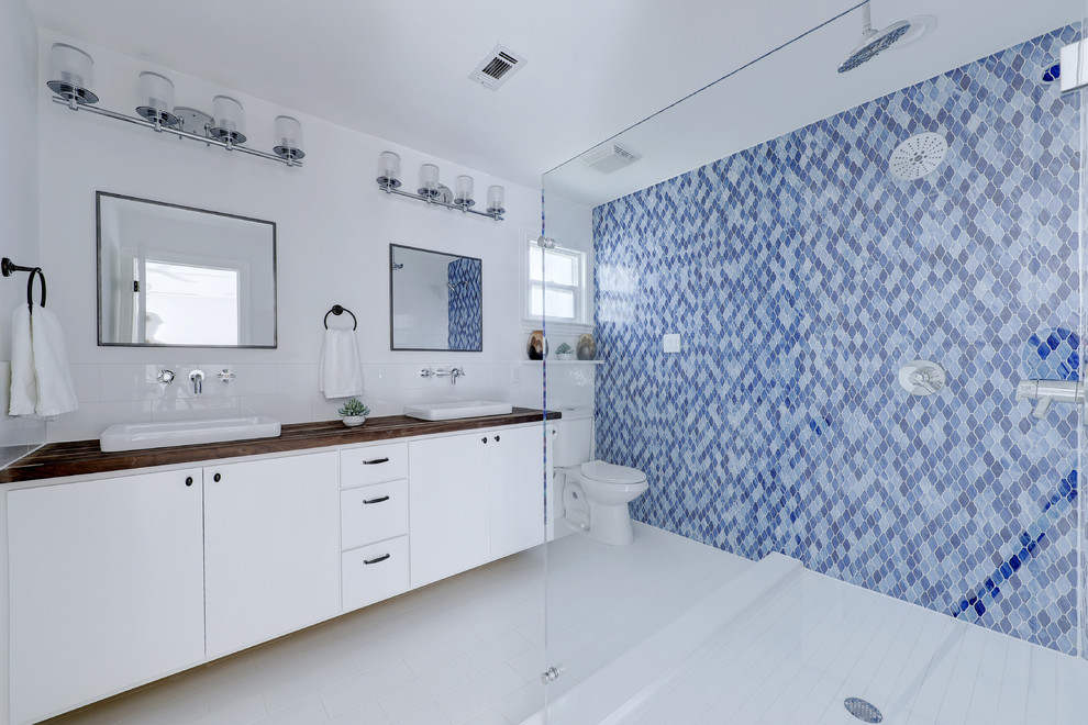 Beach style bathroom in Austin with flat-panel cabinets, white cabinets, a double shower, a two-piece toilet, mosaic tile, blue walls, a vessel sink, wood benchtops, white floor, an open shower and brown benchtops.