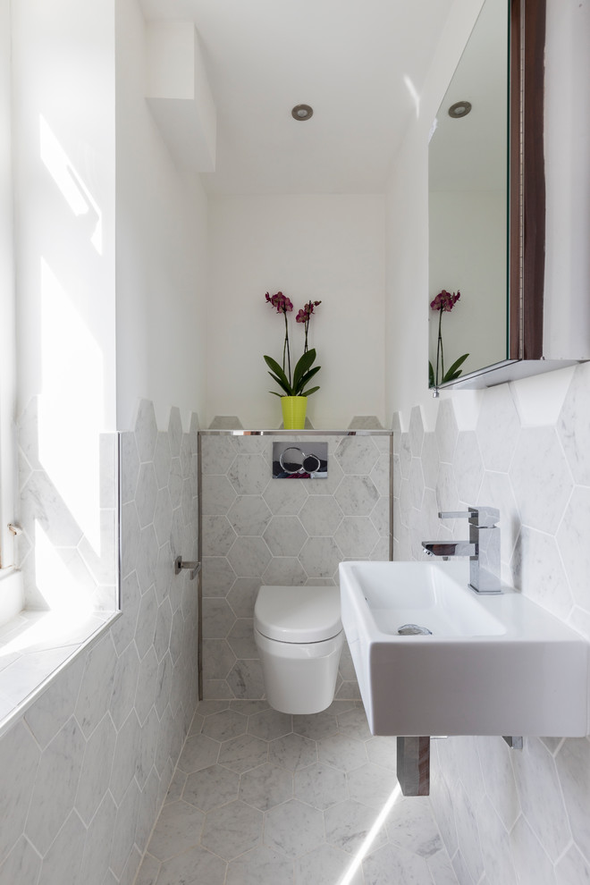 This is an example of a mid-sized modern 3/4 bathroom in London with glass-front cabinets, grey cabinets, a drop-in tub, a wall-mount toilet, beige tile, porcelain tile, beige walls, porcelain floors, a pedestal sink and wood benchtops.