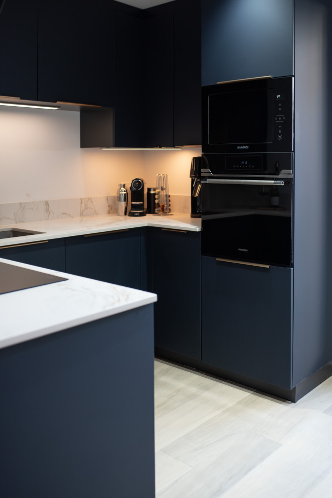 This is an example of a mid-sized contemporary u-shaped separate kitchen in Paris with an undermount sink, beaded inset cabinets, blue cabinets, solid surface benchtops, beige splashback, black appliances, light hardwood floors, with island, beige floor and beige benchtop.