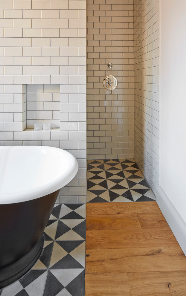 This is an example of a mid-sized scandinavian master bathroom in London with a wall-mount sink, wood benchtops, a freestanding tub, an open shower, black tile, cement tile, grey walls and medium hardwood floors.
