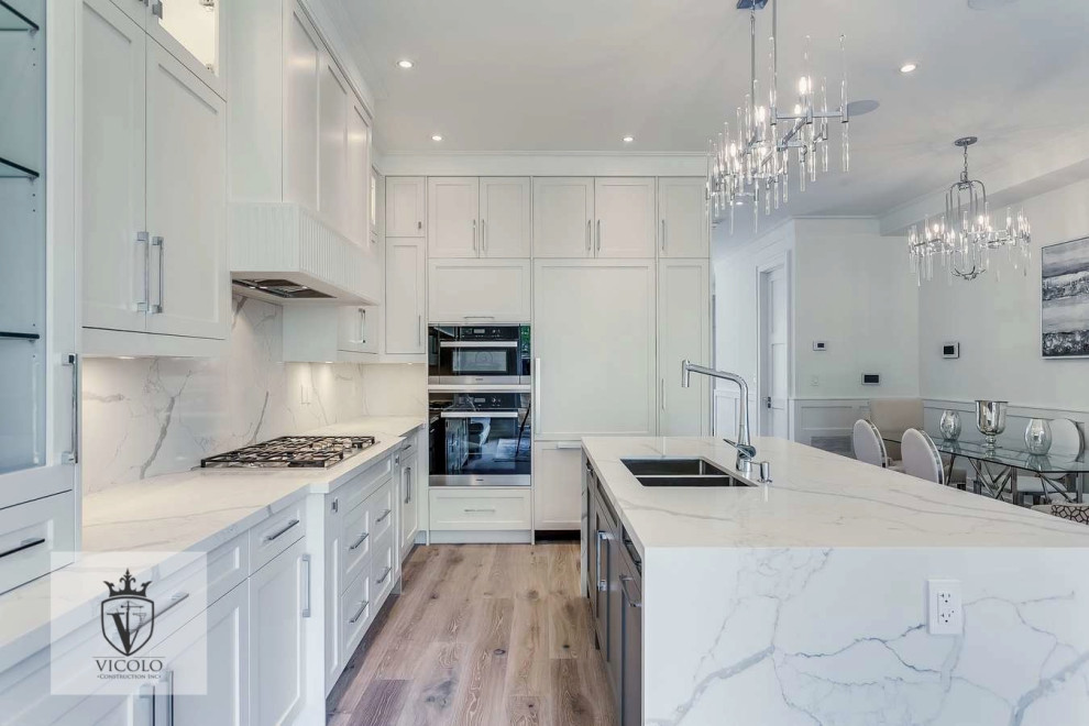 Photo of a medium sized classic grey and white l-shaped enclosed kitchen with a double-bowl sink, shaker cabinets, white cabinets, quartz worktops, white splashback, integrated appliances, light hardwood flooring, an island, brown floors, white worktops, a coffered ceiling and feature lighting.