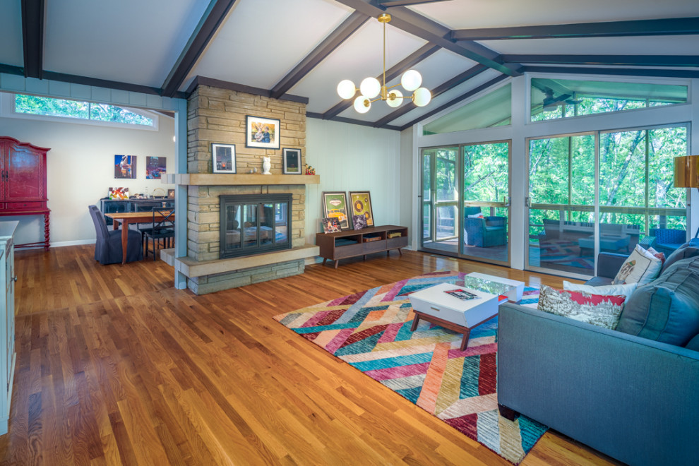 Photo of a large midcentury enclosed living room in Nashville with medium hardwood floors, a two-sided fireplace, a stone fireplace surround and exposed beam.