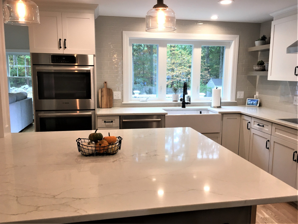 Eat-in kitchen - large transitional u-shaped light wood floor and brown floor eat-in kitchen idea in Boston with a farmhouse sink, shaker cabinets, white cabinets, quartz countertops, beige backsplash, subway tile backsplash, stainless steel appliances, an island and white countertops